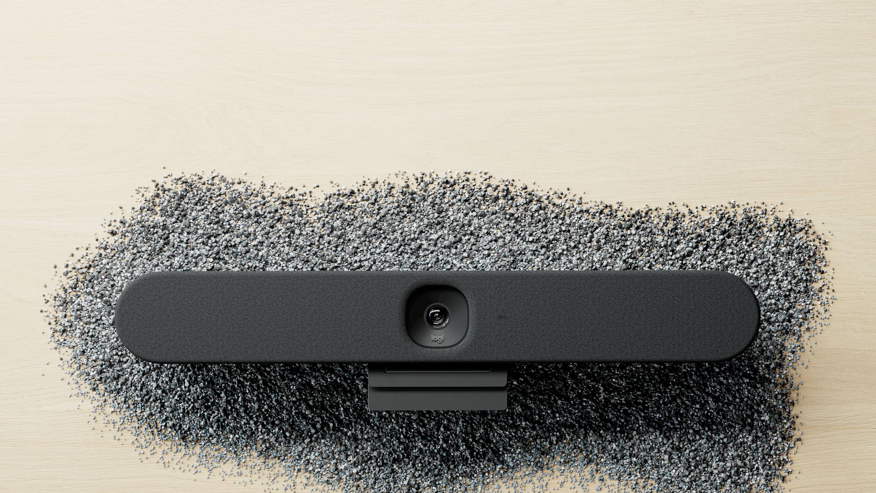 Haut-parleur noir oval sur une table claire, entouré de particules sombres et dispersées de petite taille.