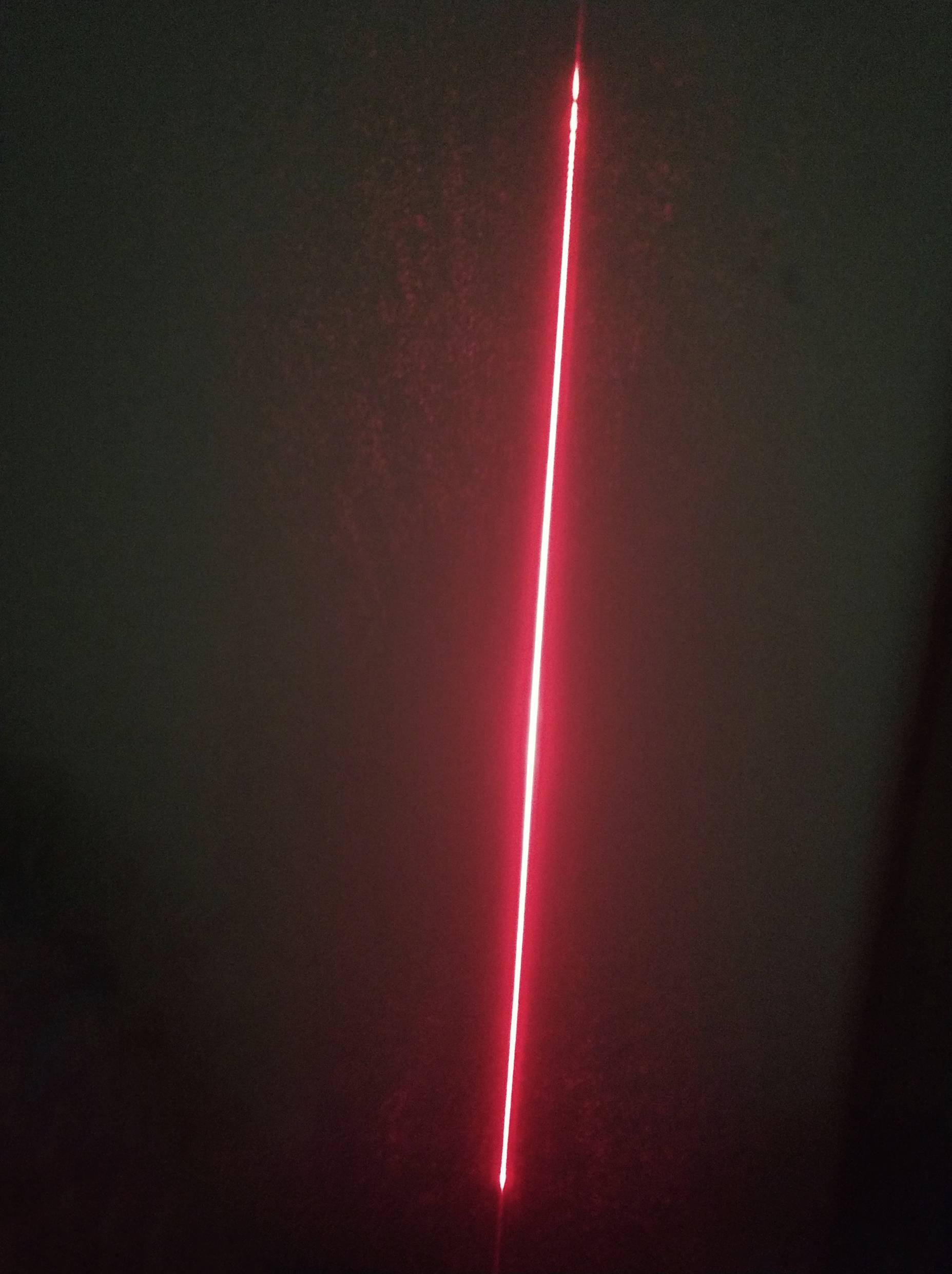 Un rayon laser rouge brille verticalement dans une pièce sombre, se détachant sur le fond sombre.