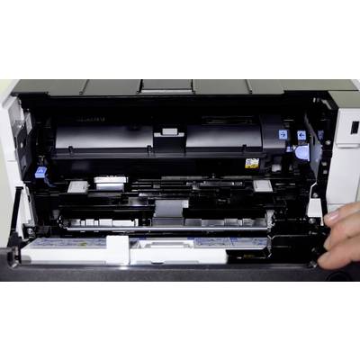Une imprimante ouverte montre son système d'alimentation papier interne et ses zones de maintenance. Une main maintient le capot ouvert.