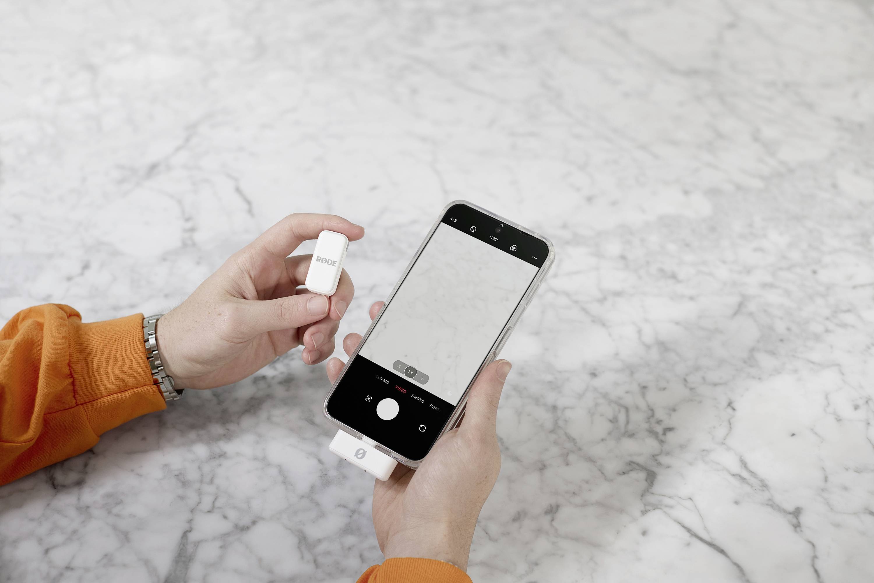 Une personne tient un smartphone avec l'application photo ouverte et connecte un appareil blanc au téléphone. Un fond de marbre est mis en évidence.