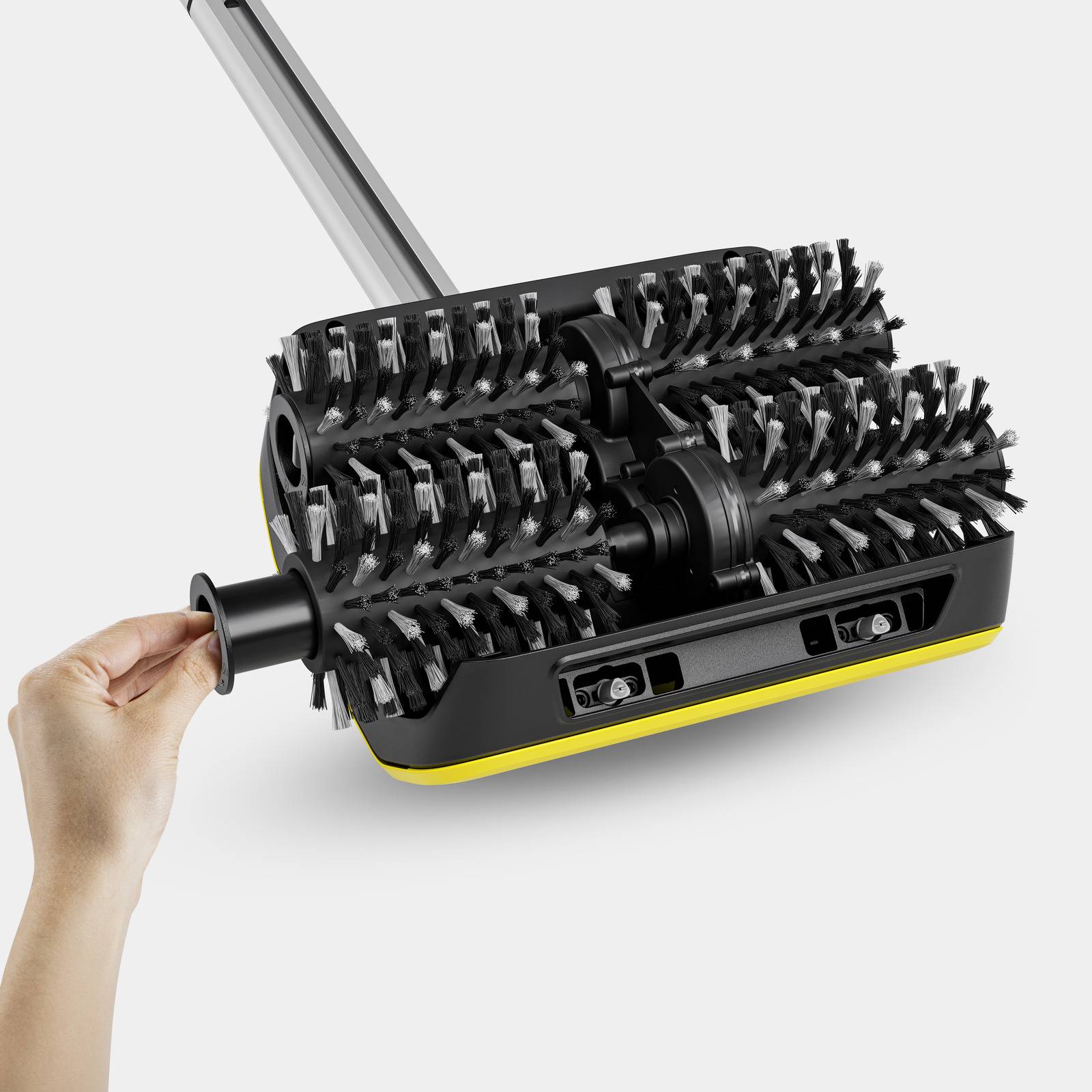 Une main ajuste une brosse de nettoyage noire avec des accents jaunes sur un fond blanc.
