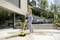 Une femme nettoie des carreaux de terrasse avec un appareil de nettoyage électrique. En arrière-plan, une terrasse moderne avec des plantes et des meubles.