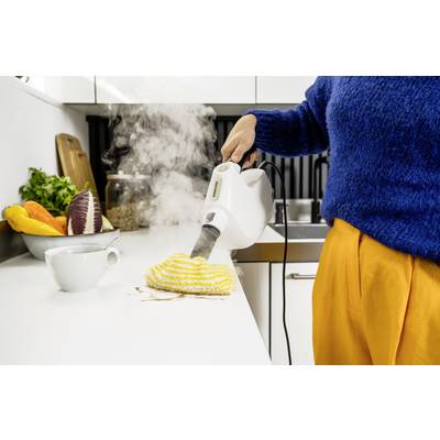 Une personne nettoie un plan de travail de cuisine sale à l'aide d'un nettoyeur vapeur. Des légumes frais sont disposés dans un bol à côté.