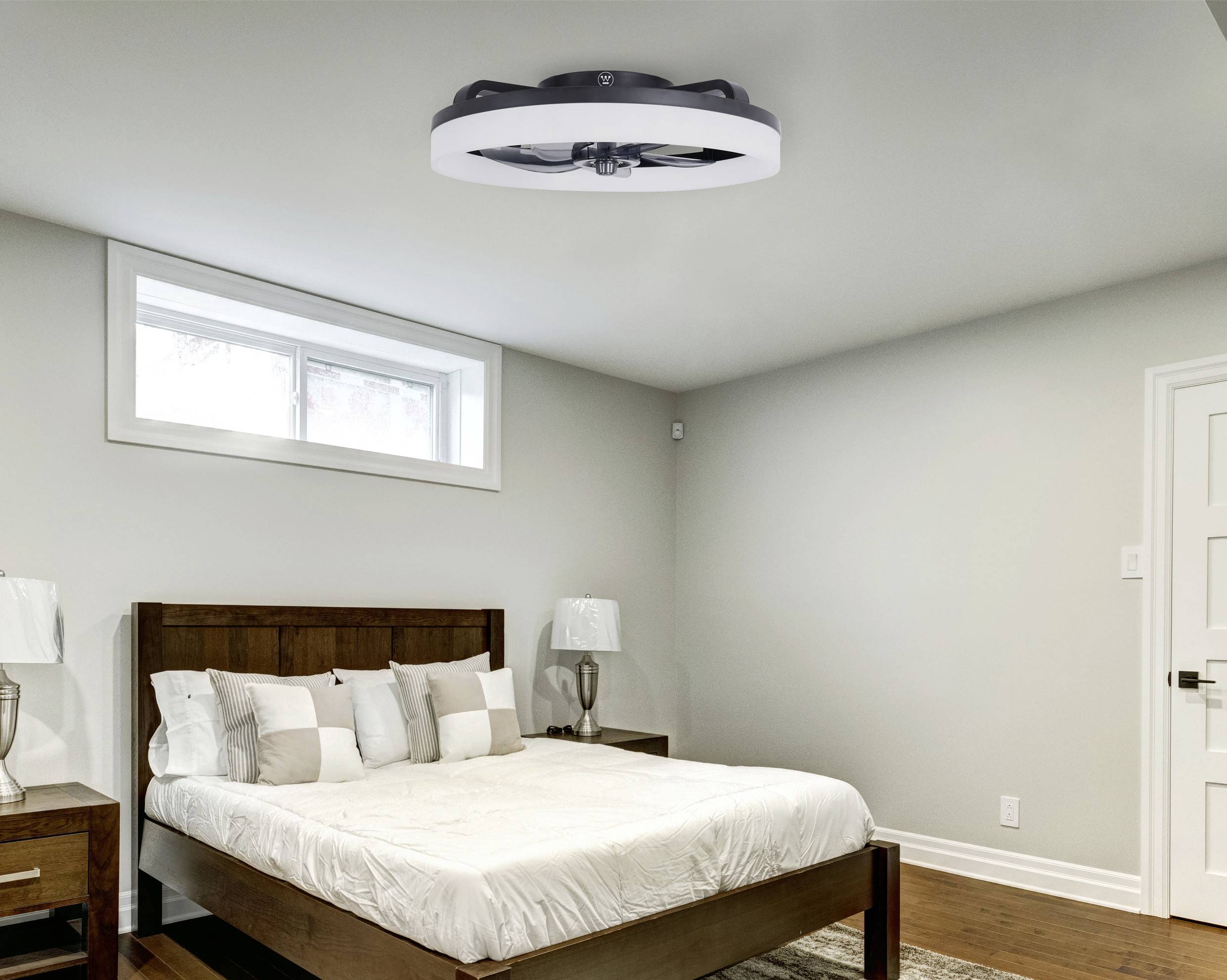 Chambre lumineuse avec un ventilateur de plafond moderne et un lit double, entourée de coussins blancs et de meubles en bois.