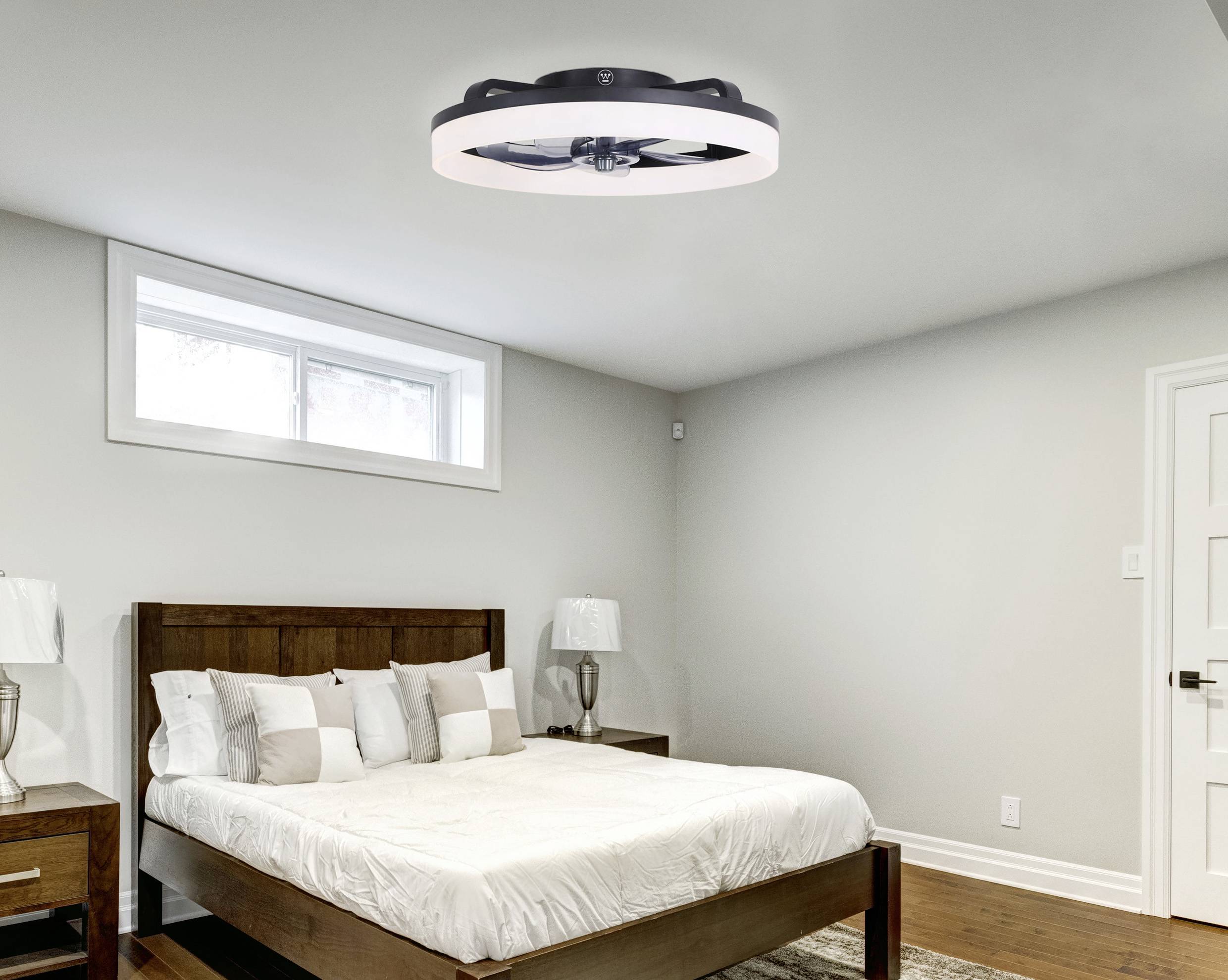 Chambre à coucher avec un grand lit, des meubles en bois et un ventilateur de plafond moderne. Une fenêtre laisse entrer la lumière du jour.