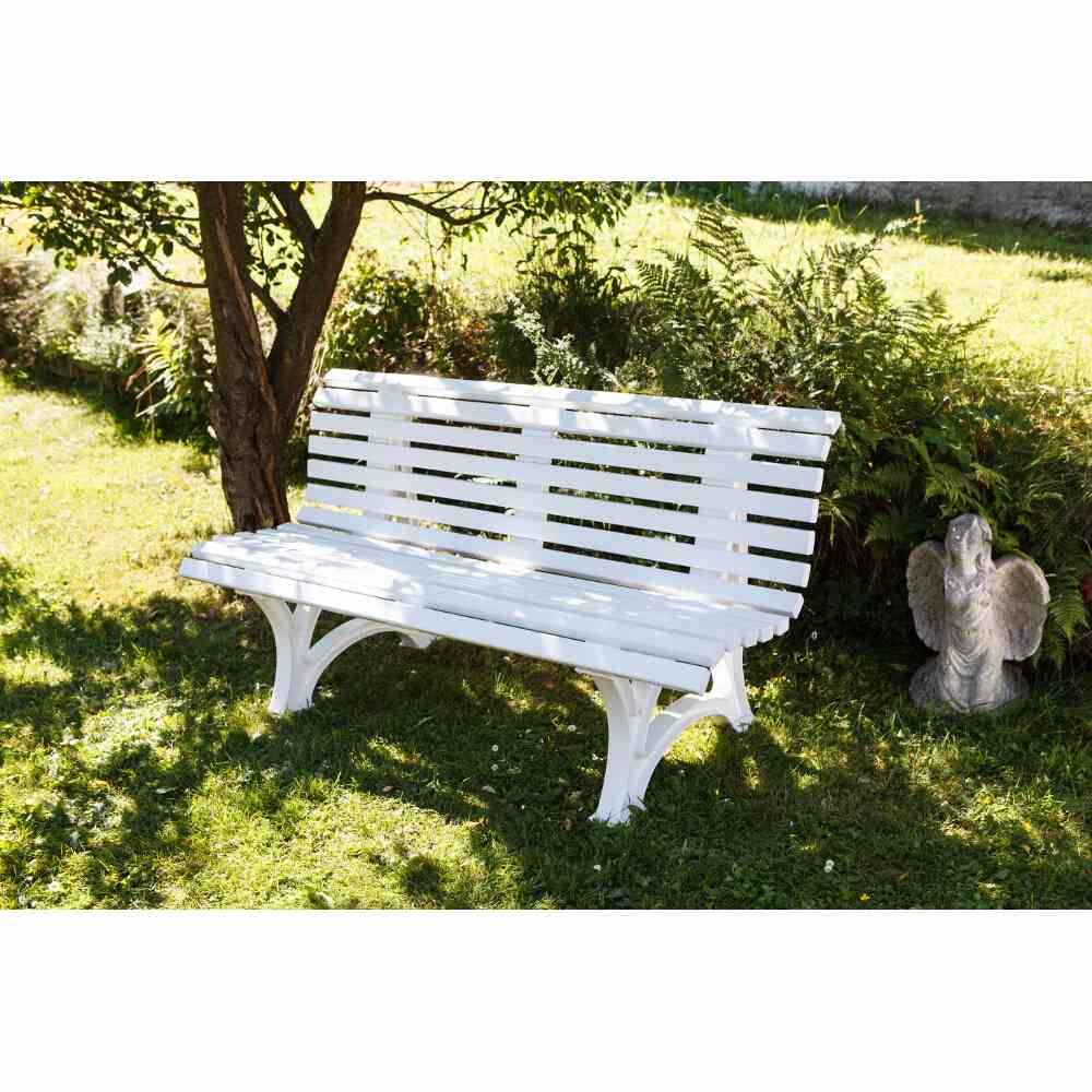 Un banc de jardin blanc est placé à l'ombre d'un arbre sur une pelouse verte. À sa droite se trouve une petite statue décorative.