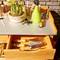 Espace de travail de jardin avec un pot de narcisses, des traces de terre, un arrosoir, de petits outils et des étiquettes de plantes sur une table.
