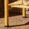 Banc en bois sur une terrasse en briques, partiellement éclairé par le soleil. Un seau argenté est posé sur le côté droit du banc.