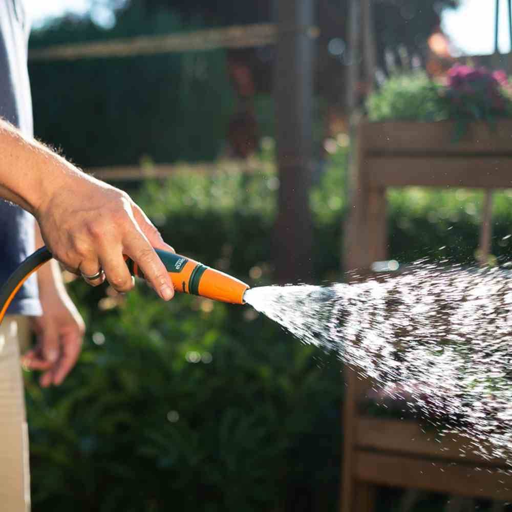 Une personne arrose des plantes avec un tuyau d'arrosage dans un jardin ensoleillé.