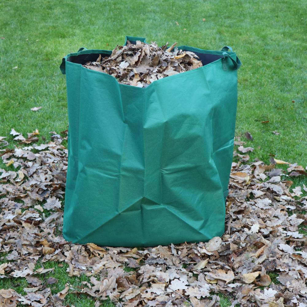 Sac de jardin vert rempli de feuilles d'automne sur une pelouse, entouré de feuilles tombées.