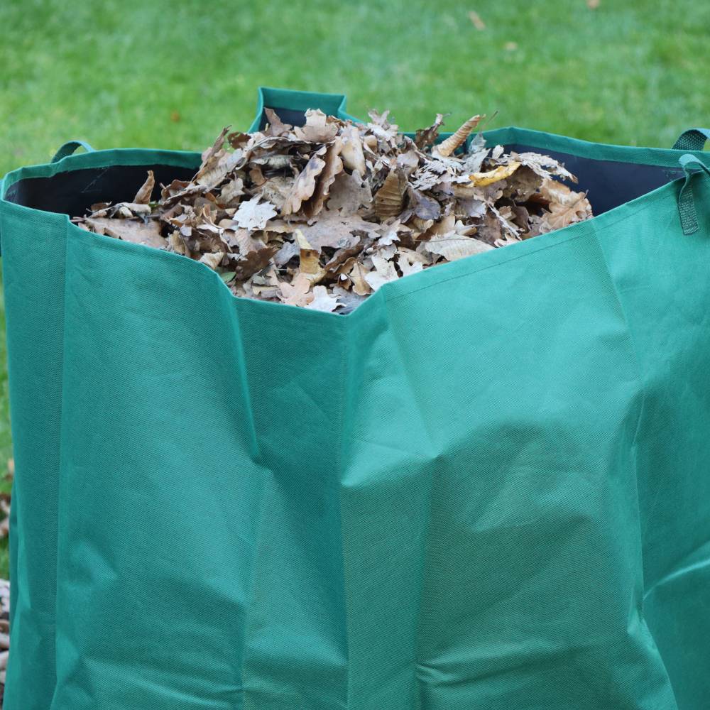 Un grand sac vert est rempli de feuilles d'automne et se trouve sur la pelouse du jardin.