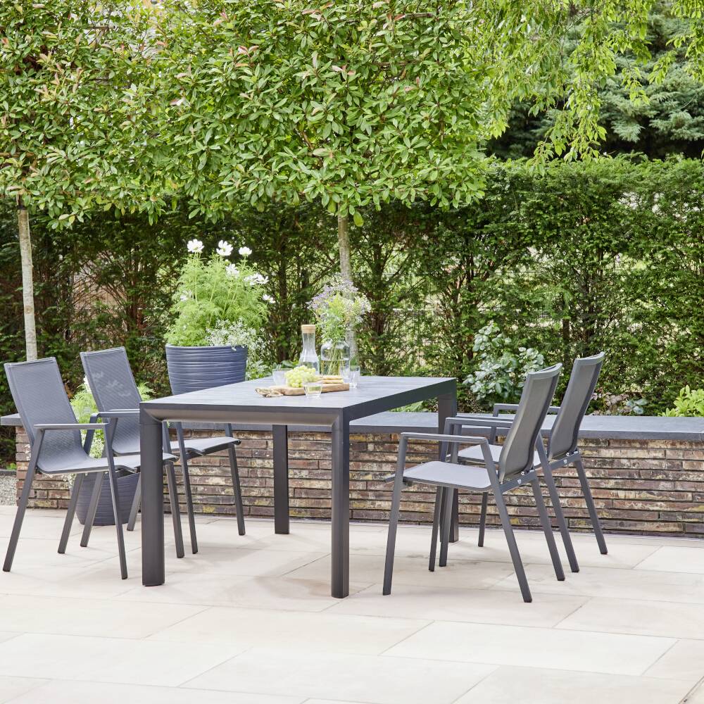Un ensemble de meubles de jardin composé d'une table et de six chaises est installé sur une terrasse. Des arbustes et des arbres sont visibles en arrière-plan.
