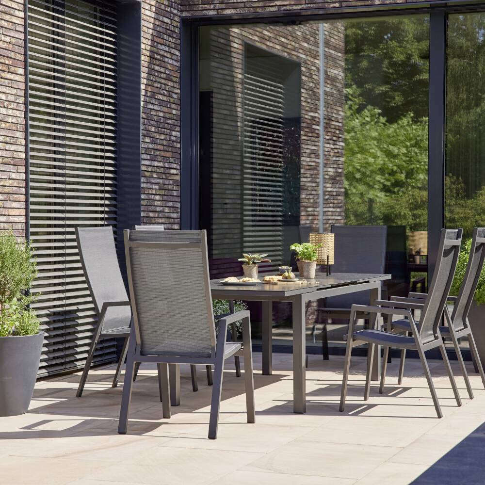 Terrasse avec table à manger, six chaises et plantes décoratives en pot. La porte coulissante vitrée en arrière-plan offre une vue sur l'intérieur.