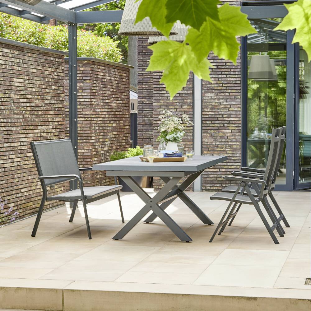 Un jardin moderne avec une table à manger en métal et six chaises sur une terrasse lumineuse, entouré de hauts murs de briques.