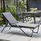 Jardin avec un transat gris moderne à l'avant-plan, entouré d'une table et de quatre chaises. Des plantes et un pare-vue dans le fond.
