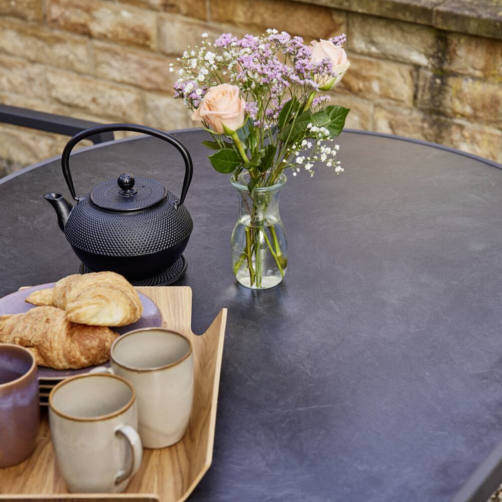 Une table ronde avec une cruche de thé, deux croissants, trois tasses et un bouquet de fleurs dans un vase. Arrière-plan en pierre.