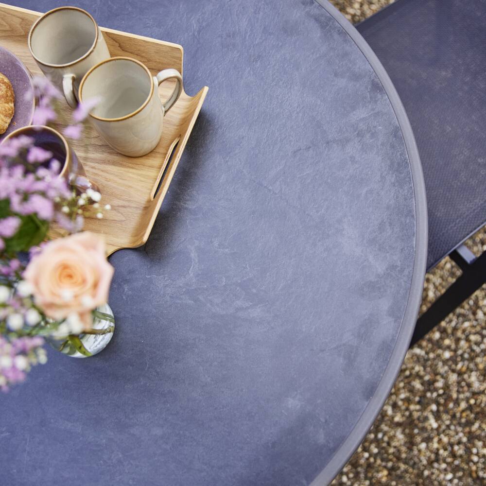 Une surface de table ronde grise avec un plateau sur lequel sont posées deux tasses. Au premier plan, un bouquet de fleurs aux pétales roses et mauves.