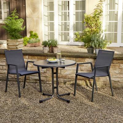 Deux chaises et une table ronde sur un sol de gravier devant un muret bas en pierre avec des plantes. Sur la table, il y a des verres et de l'eau.