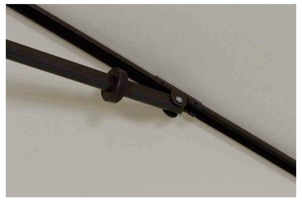 Tringle à rideaux en gros plan, fixée à un mur peint en blanc. Métal foncé avec élément de fixation, vue de côté.