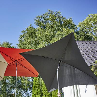 Deux grands parasols offrant de l'ombre, l'un rouge, l'autre gris, dans un jardin ensoleillé. En arrière-plan, des arbres verts et un toit de maison.