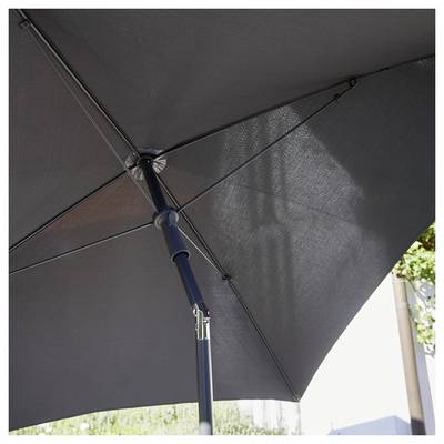 Un grand parasol gris s'étend sur un espace extérieur. Le soleil filtre légèrement à travers le tissu du parasol.