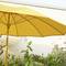 Un parasol jaune est ouvert dans un jardin, entouré de diverses plantes vertes et de fleurs mauves.