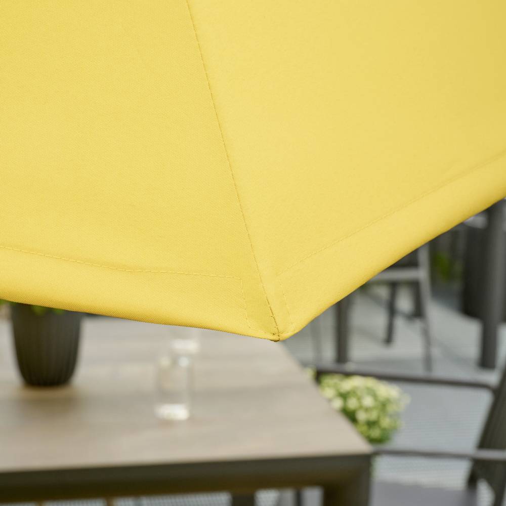 Un store jaune recouvre partiellement une table extérieure avec des chaises. Des plantes sont visibles en arrière-plan.