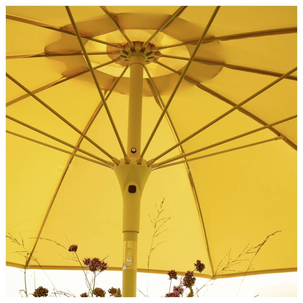 Parasol jaune photographié du dessous, montrant le mécanisme et les branches. Des plantes sont visibles en arrière-plan.
