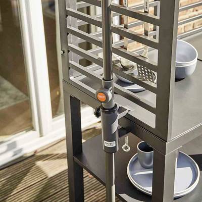 Une table en métal noir avec un support intégré pour ustensiles de barbecue sur une terrasse. Sur la table, de la vaisselle bleue est disposée.