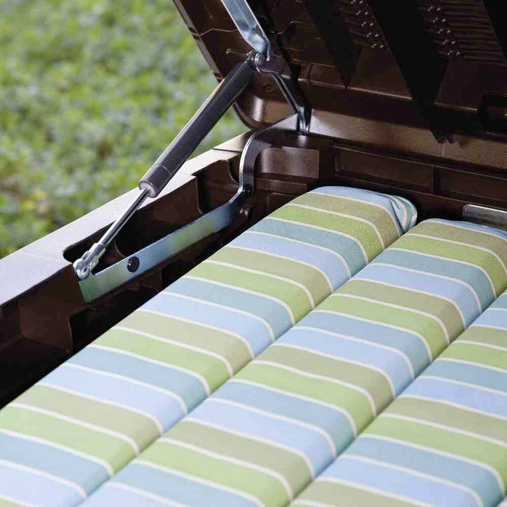 Un coffre de banc de jardin ouvert contenant des coussins d'assise rayés dans différentes nuances de vert, prêts à être utilisés en extérieur.