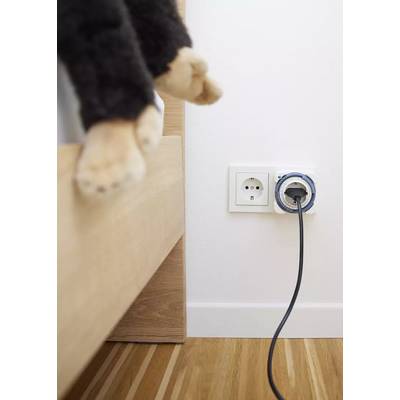 Une patte de chat à côté d'un lit, près d'une prise électrique d'où dépasse un câble noir.