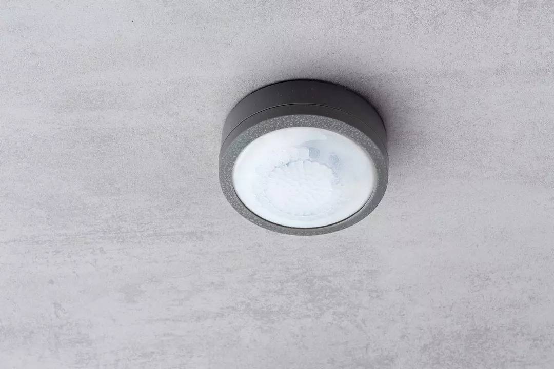 Une lampe de plafond ronde grise avec un diffuseur en verre dépoli, fixée à un plafond gris.