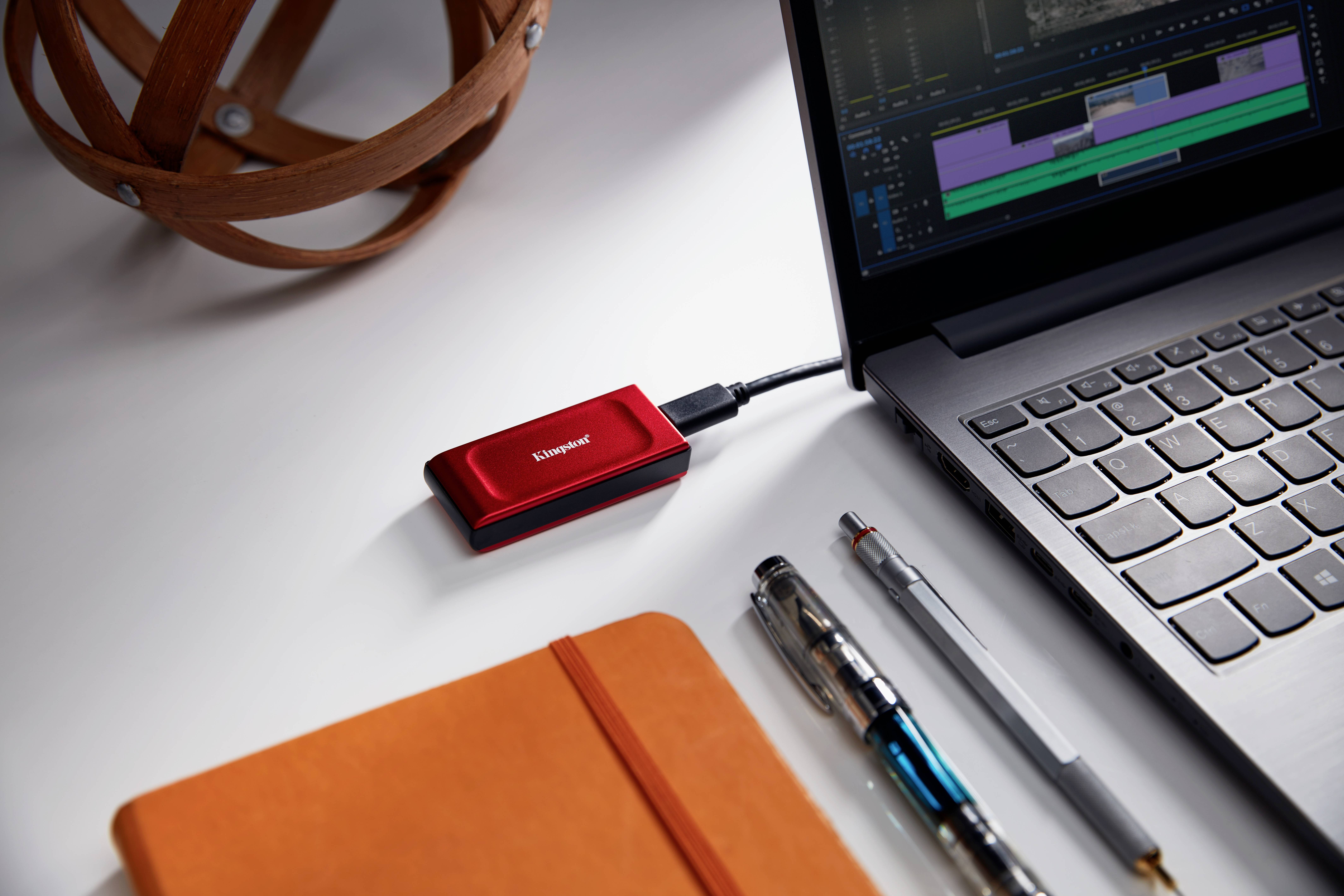 Un périphérique de stockage externe rouge est connecté à un ordinateur portable. Des logiciels de montage vidéo sont ouverts sur l'écran de l'ordinateur portable.