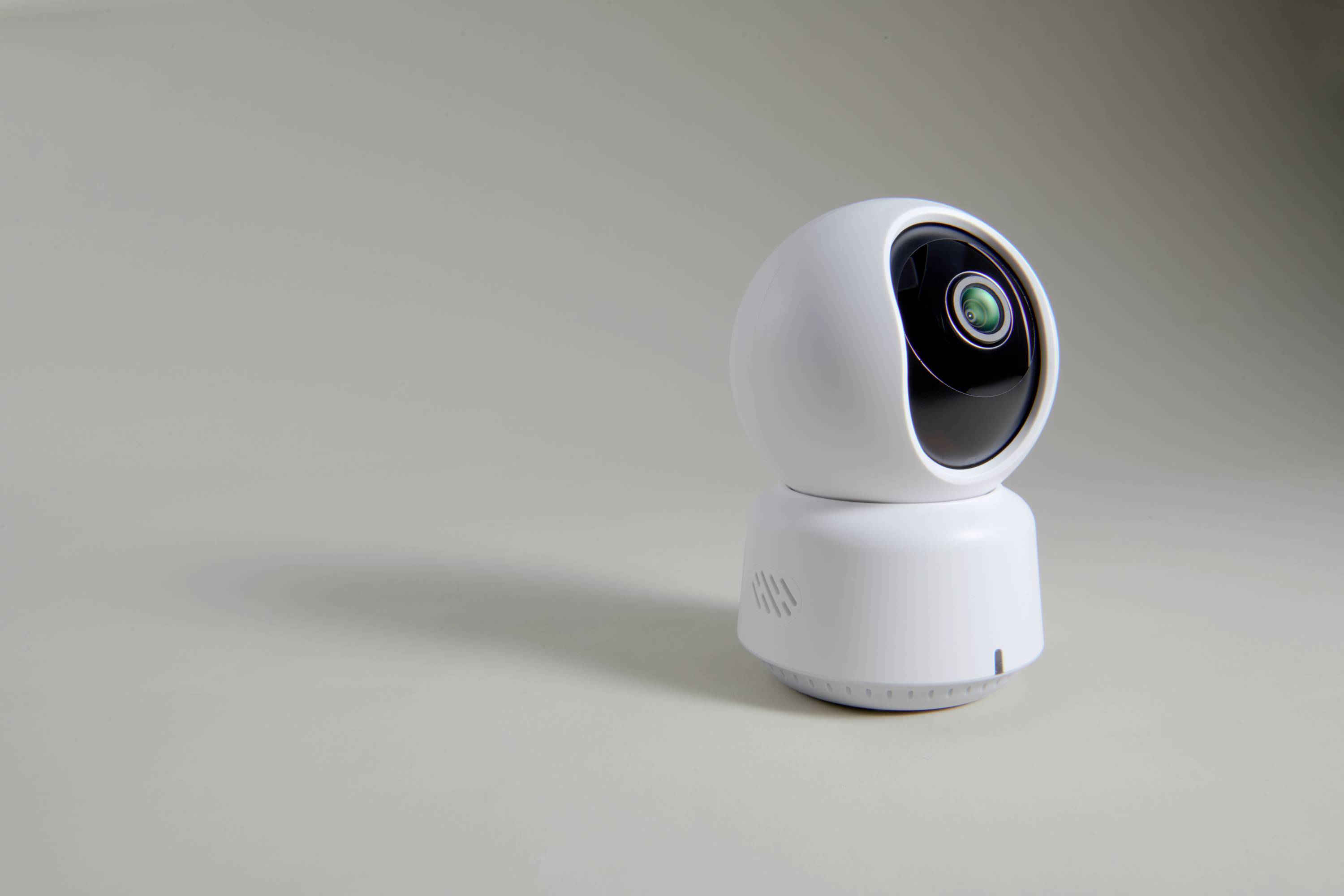 Caméra de surveillance blanche au design sphérique, orientée vers la droite sur un fond gris. Elle est destinée à la sécurité et à la surveillance des locaux.