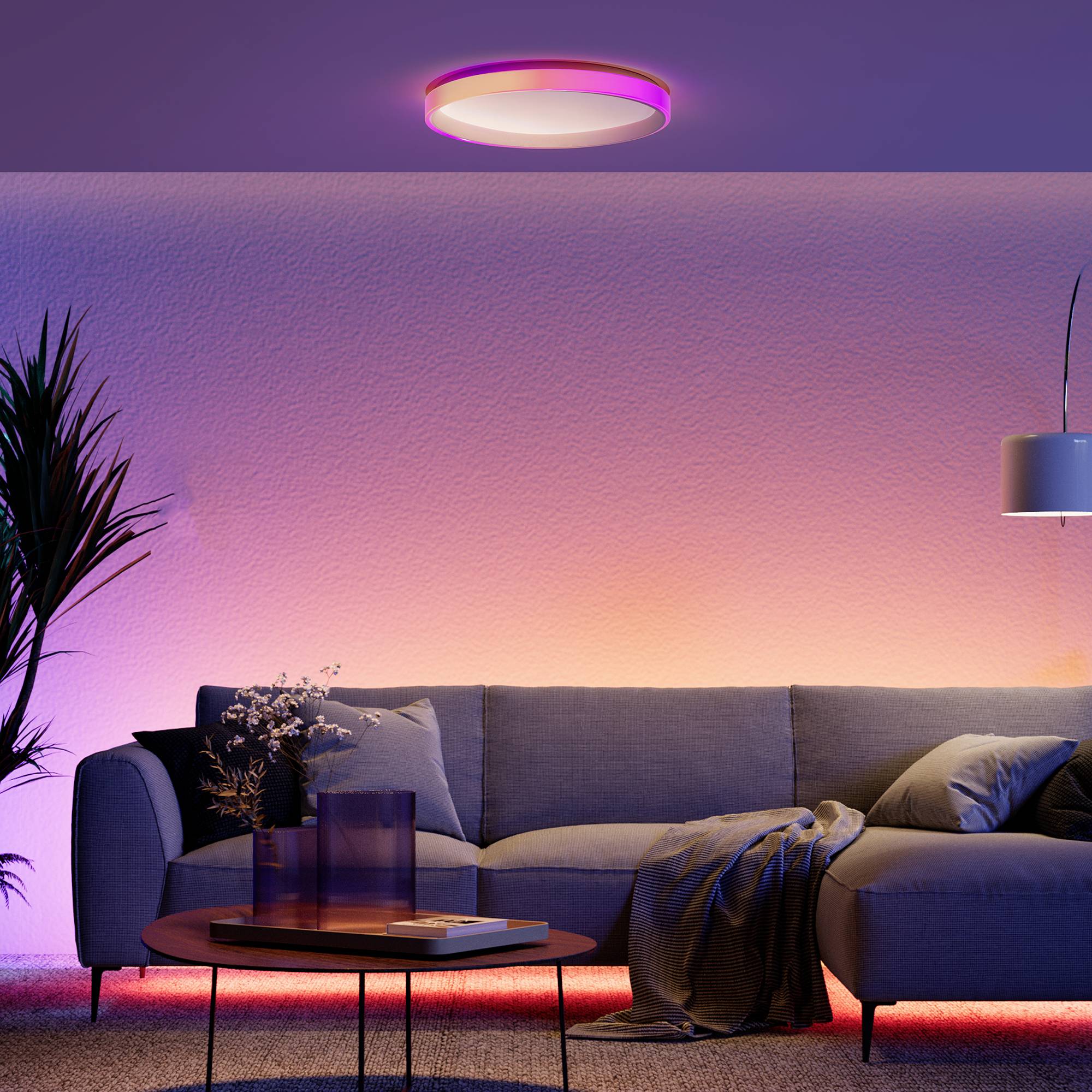 Salon avec éclairage moderne : Lustre rond au plafond diffusant une lumière violette, éclairage mural orange. Canapé bleu, table d'appoint.