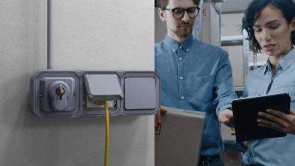 Un homme et une femme dans un bureau vérifient ensemble des informations sur une tablette. Au premier plan, une prise électrique avec un câble.
