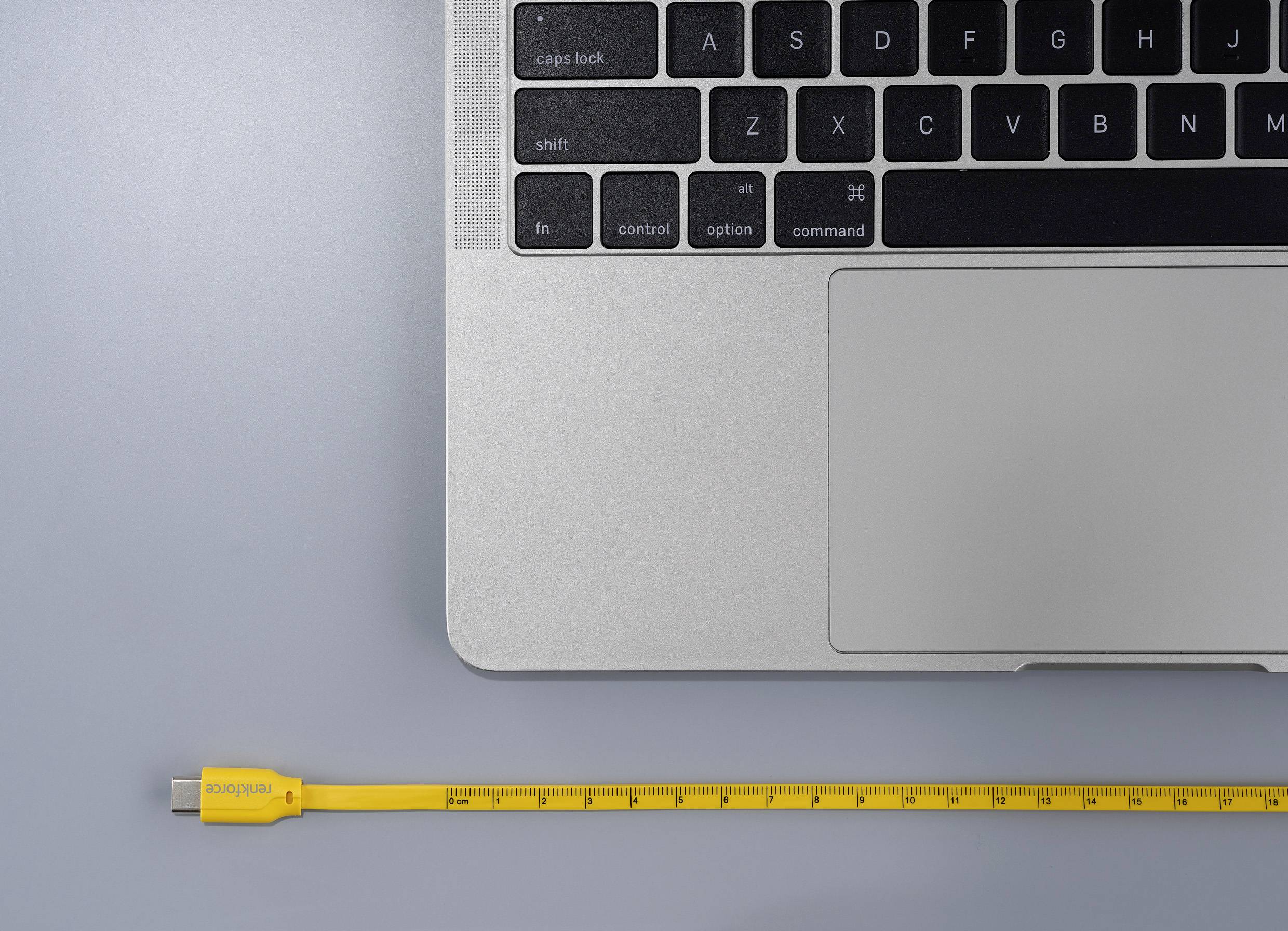 Un ordinateur portable avec clavier sur un fond gris. À côté se trouve un câble USB jaune conçu comme un mètre ruban.