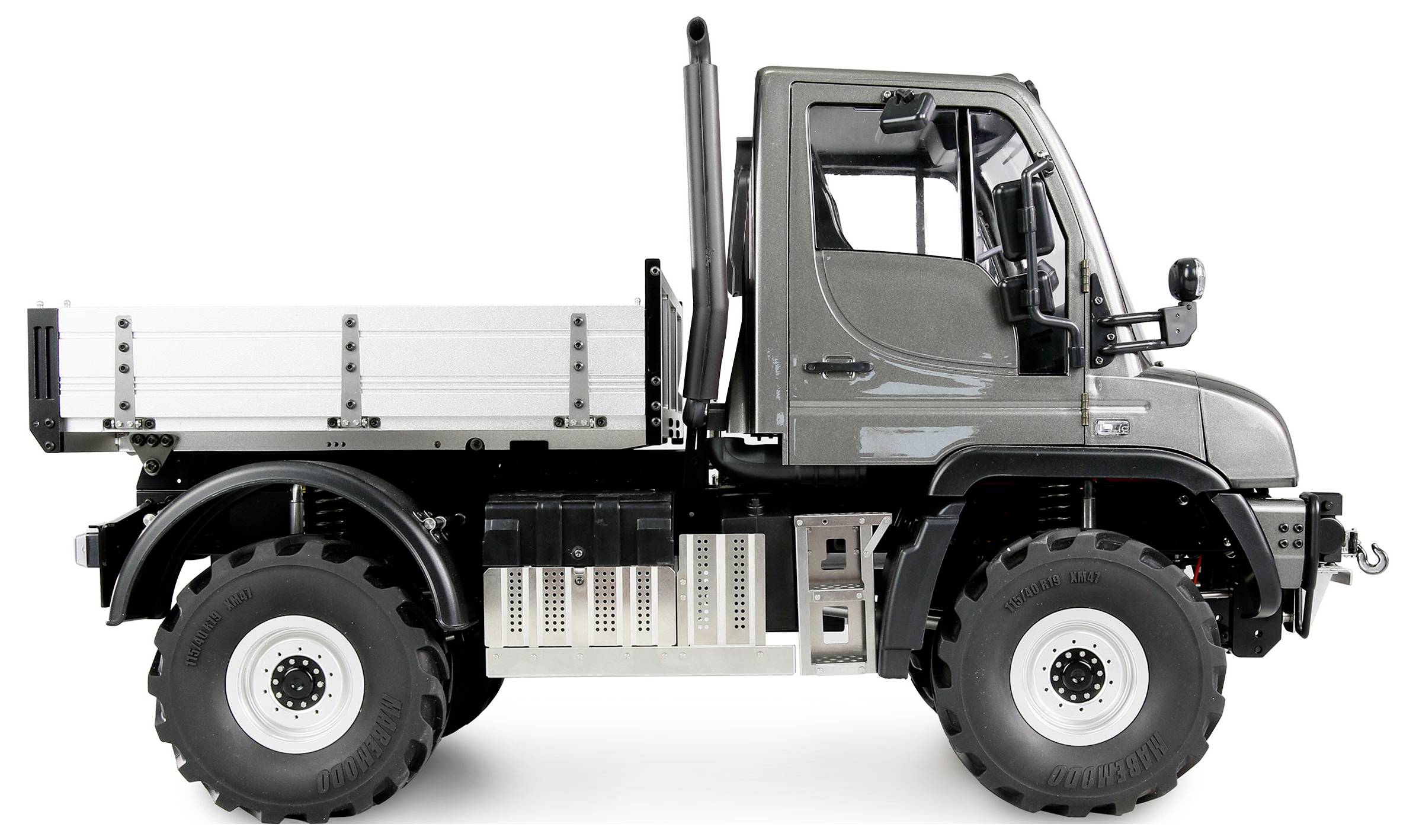 Camion gris avec une petite surface de chargement et de grandes roues, vue latérale. Le véhicule est haut, robustement construit et adapté aux terrains accidentés.