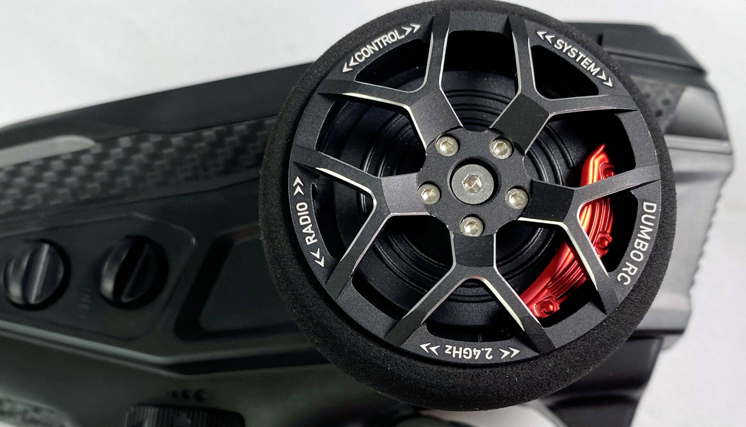 Un volant noir avec un accent rouge sur un appareil portant les mentions 'CONTROL', 'SYSTEM', 'RADIO' et 'DUMBORC'.