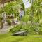 Une personne se tient dans un jardin à côté de fleurs et de plantes, entourée de feuillage vert. Un projecteur solaire est visible au premier plan.