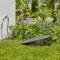 Une pelouse de jardin tondue avec une tondeuse rétractable près d'une source d'eau, entourée de plantes et de fleurs par une journée ensoleillée.