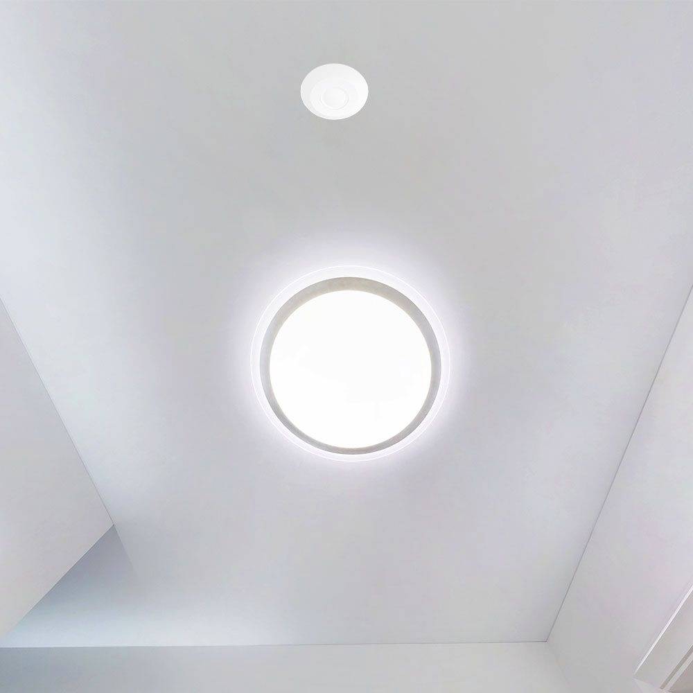 Une lampe de plafond ronde et lumineuse éclaire une pièce blanche moderne. La lampe sert de source de lumière principale.