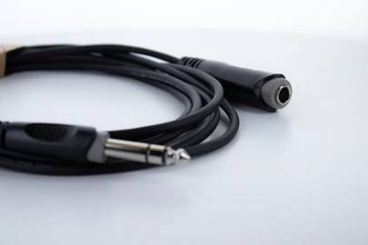 Câble audio noir avec fiches jack mâle et femelle sur fond blanc, représentation d'une connexion audio typique.