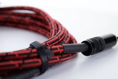 Un câble audio à motif rouge et noir, enroulé et maintenu par une sangle velcro.