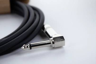 Un connecteur jack coudé à 90 degrés de 6,3 mm avec un câble noir est posé sur une surface. Adapté aux instruments de musique et aux appareils audio.