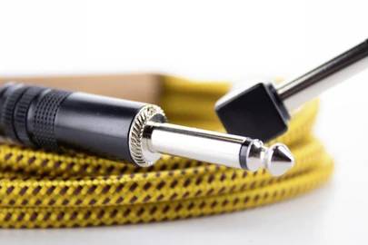 Gros plan sur un câble de guitare jaune avec des fiches noires, utilisé pour les instruments de musique.