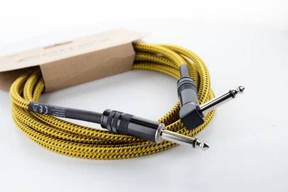 Câble audio jaune tressé avec deux fiches jack noires. Une fiche est droite, l'autre coudée. Emballage en arrière-plan.