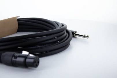 Câble audio noir avec une connectique XLR et une fiche jack sur un fond blanc, partiellement dans son emballage.