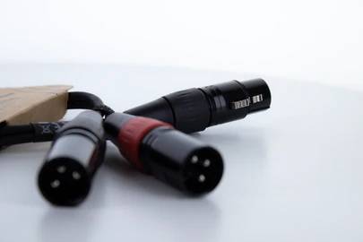 Trois fiches XLR sur une surface blanche. Deux fiches sont orientées vers l'avant, tandis qu'une fiche est tournée vers l'arrière.
