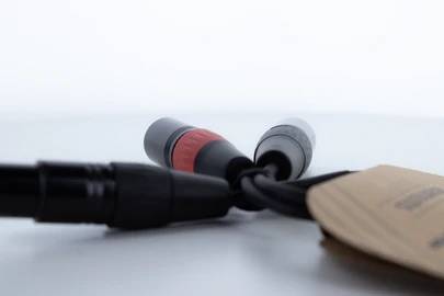 Deux câbles noirs avec des fiches reposent sur une surface blanche. Une fiche possède une bande rouge. À droite se trouve une étiquette brune.